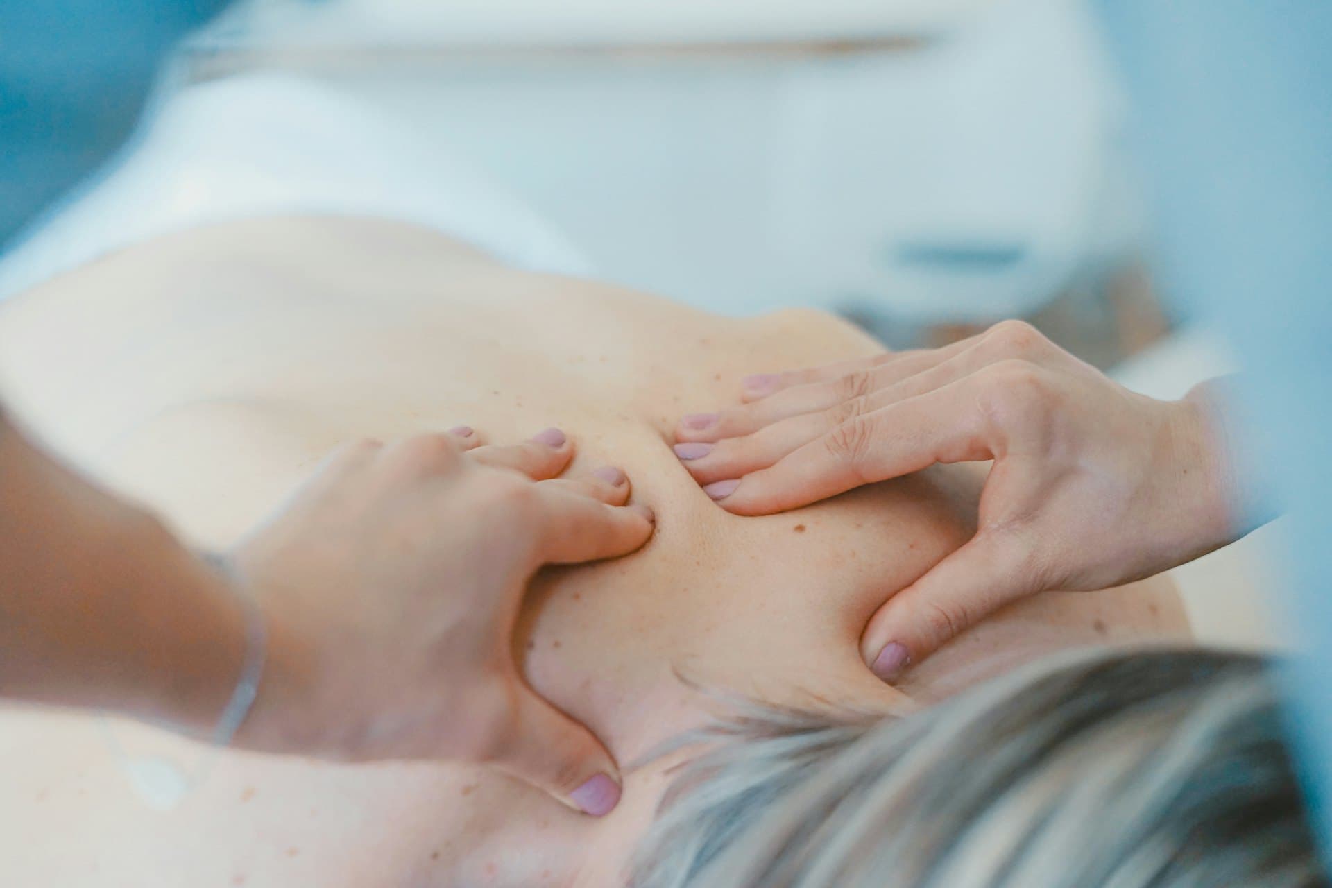 Two therapists' hands working in tandem across the shoulders